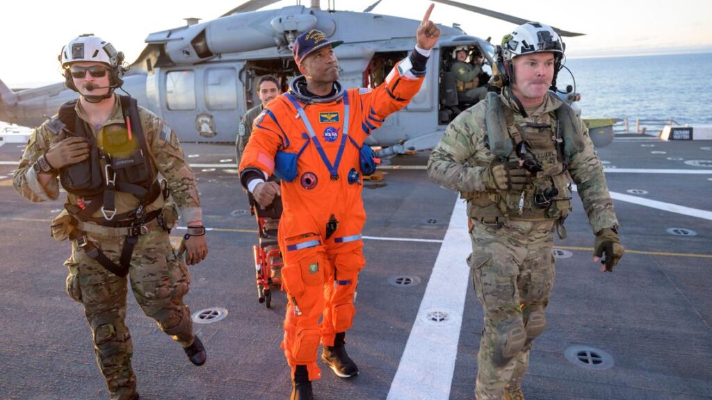 Military helicopters hoisting Artemis II astronauts from an inflatable raft in the ocean